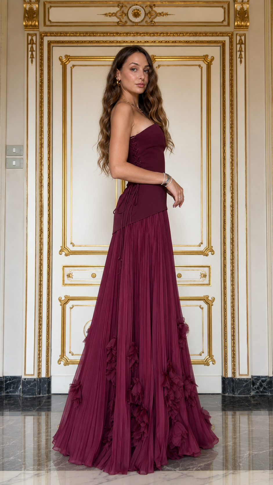 Side view of burgundy strapless pleated maxi gown with floral hem detail