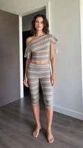 Front view of woman wearing brown striped one-shoulder crop top and capri leggings set