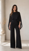 Front view of black cape sleeve wide leg jumpsuit with lace trim