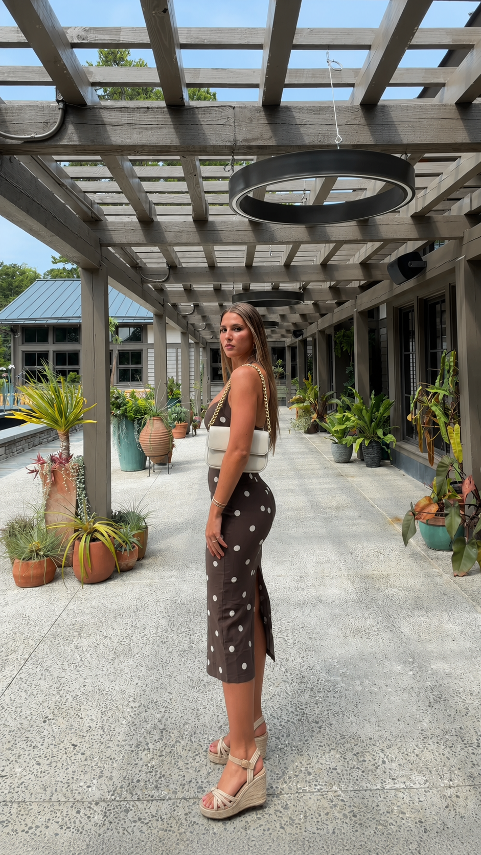 Angled side view of chocolate brown sleeveless polka dot midi dress
