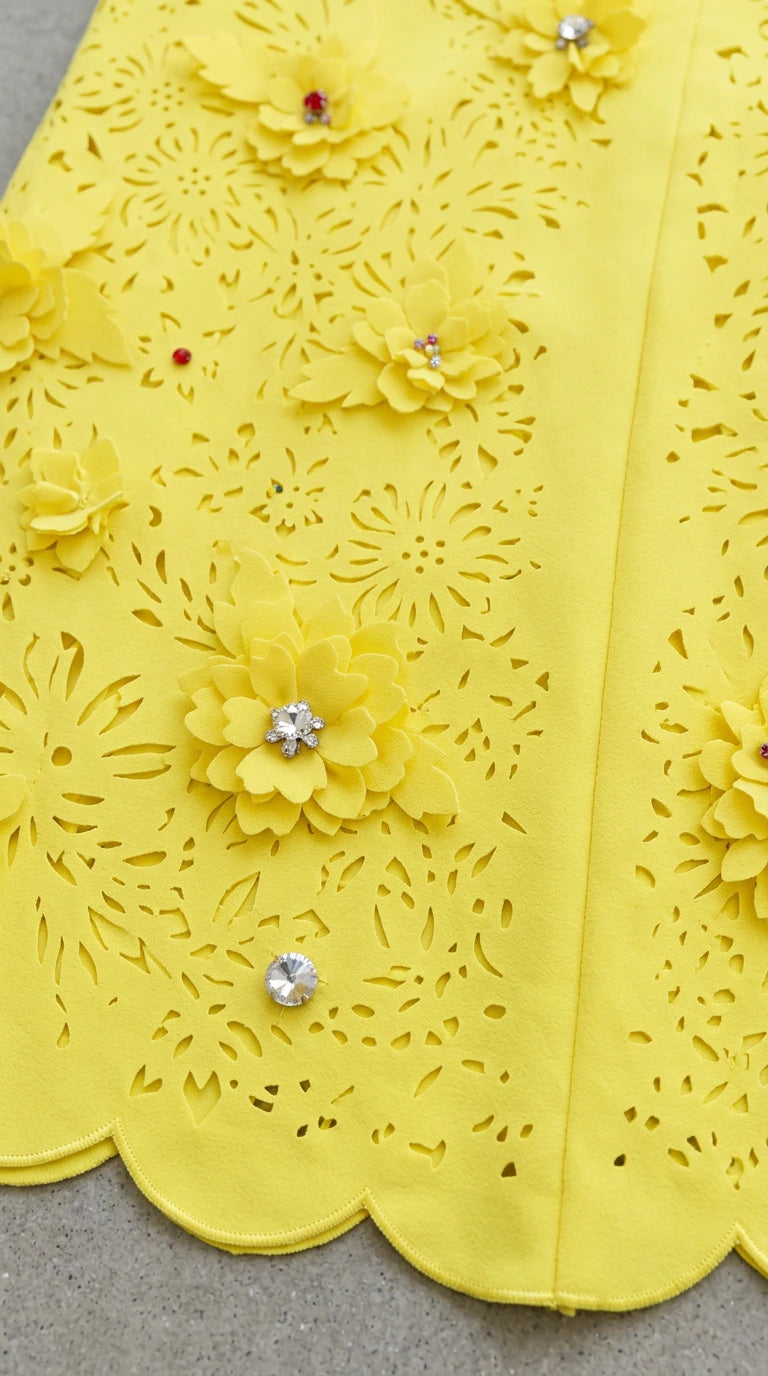 Close-up detail of yellow dress fabric showing laser-cut patterns, floral appliqués, and rhinestones