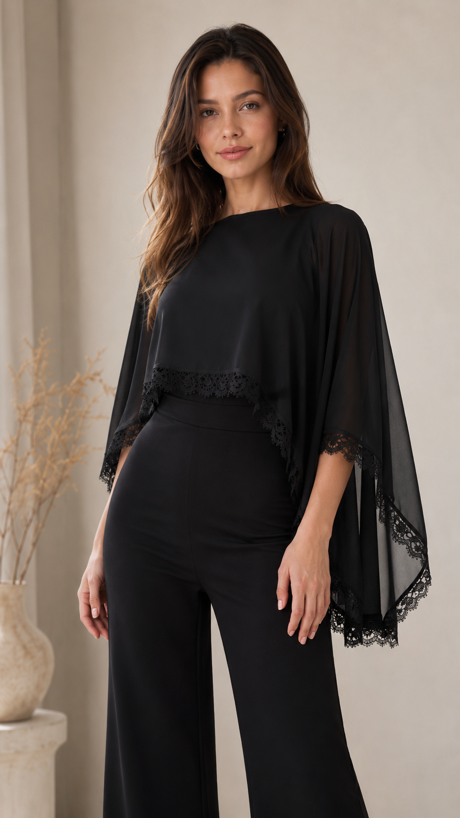 Close-up front view of black bateau neck jumpsuit with lace-trim cape sleeve detail