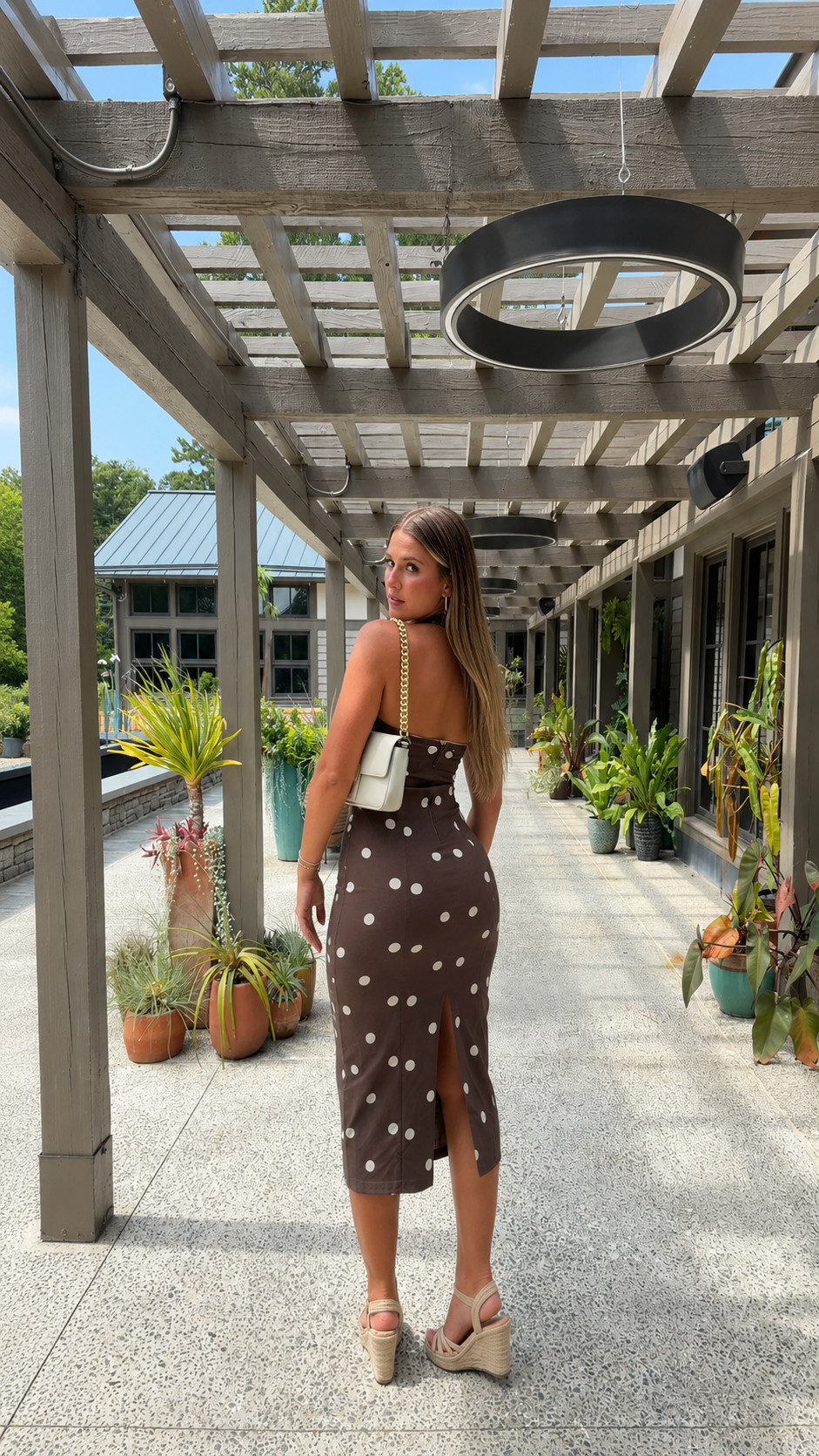 Back view of chocolate brown polka dot midi dress showing slit detail