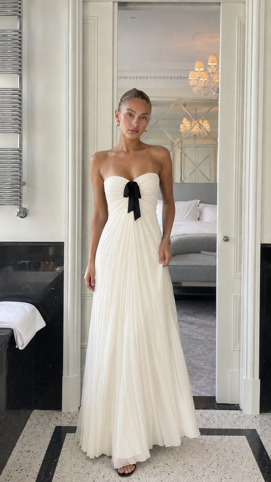 Front view of ivory strapless pleated maxi gown with black bow detail