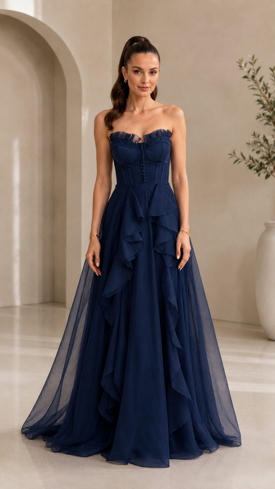 Front view of navy blue strapless formal gown with sheer overlay and layered front ruffles