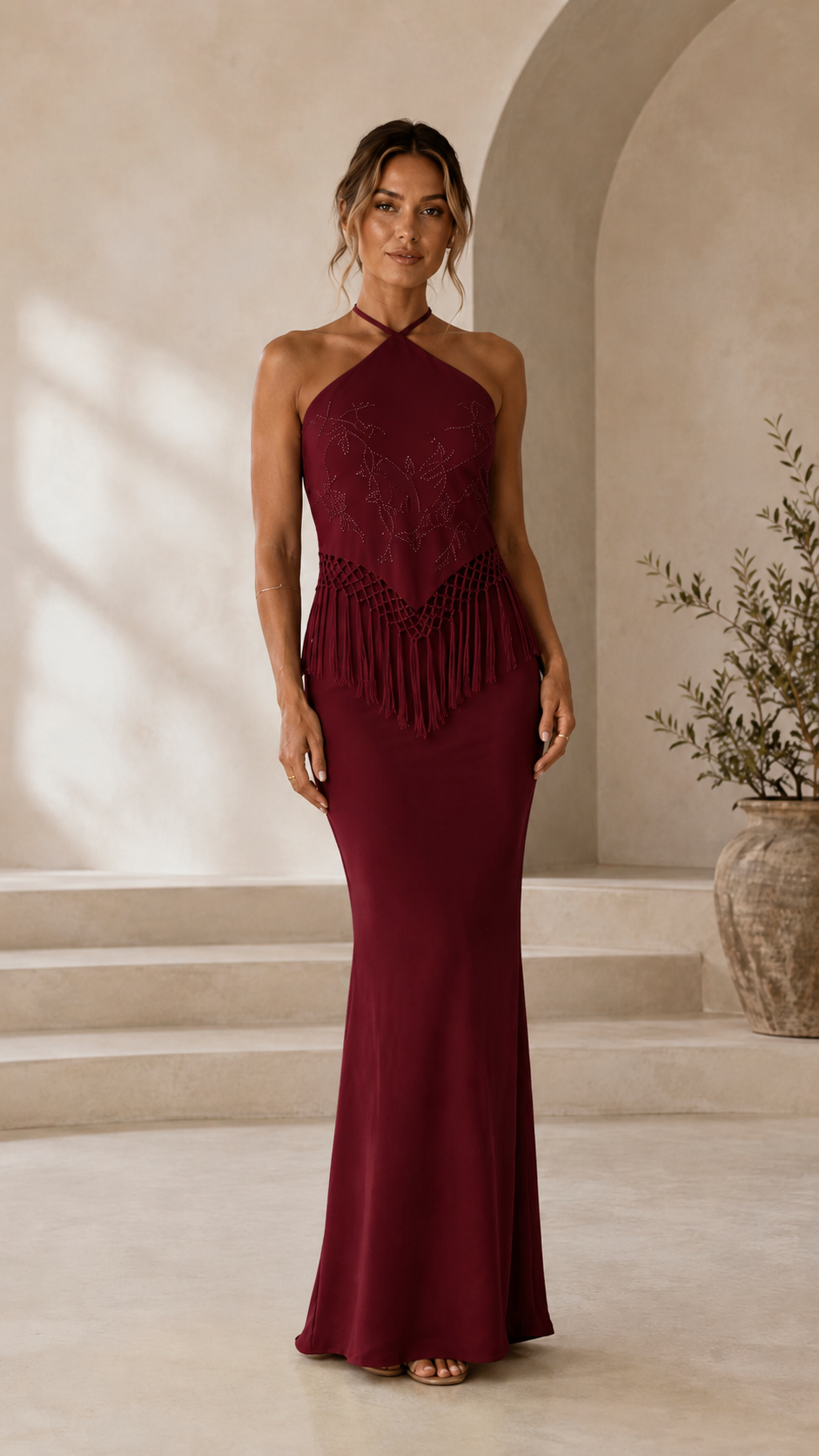 Front view of burgundy halter mermaid maxi dress with fringe waist detail